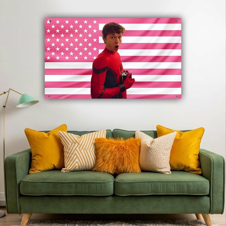 以下が含まれることがあります： ピンクと白のアメリカ国旗のデザインと、赤と黒のスーツを着た人物が描かれた額入りのウォールアート。アートは、黄色とクリーム色のクッションが付いた緑色のソファの上に飾られています。