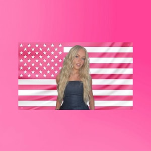 Puede incluir: Una mujer con pelo largo y rubio está delante de una bandera americana rosa. Lleva un top de mezclilla sin tirantes. La bandera tiene rayas rosas y estrellas blancas.