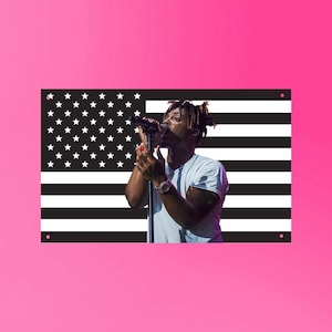 May include: A rectangular sign featuring a black and white American flag design with a photograph of a person singing into a microphone. The background is a vibrant pink.
