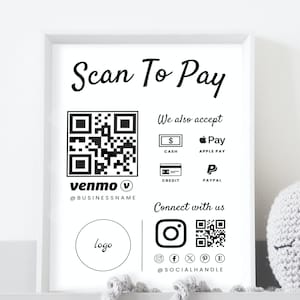 Puede incluir: Un letrero enmarcado con el texto "Scan To Pay" en negro. Incluye un código QR, el logotipo de Venmo e iconos para efectivo, crédito, Apple Pay y PayPal. El letrero también presenta iconos de redes sociales.