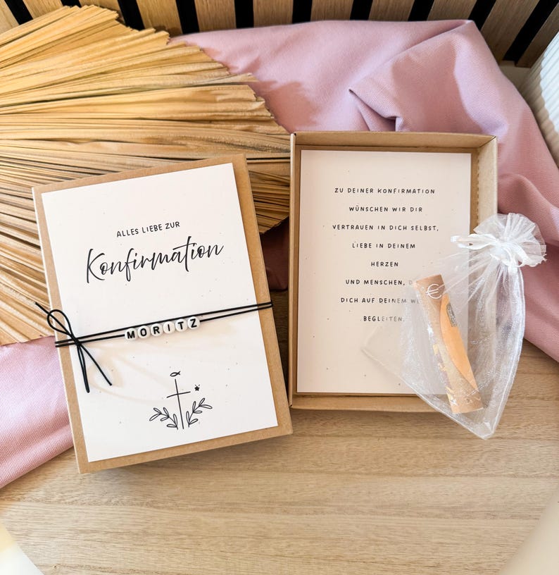 May include: A Confirmation gift set featuring a greeting card with the word "Konfirmation" and the name "MORITZ". The set includes a small gift in a sheer bag and a card with text inside a box.