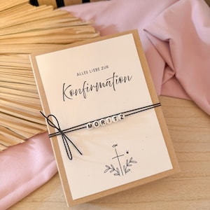 May include: A greeting card with the words "Alles Liebe zur Konfirmation" and the name "MORITZ" spelled out in white beads. The card is tied with black string and features a cross and leaf design.
