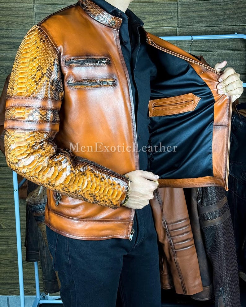 May include: A brown leather jacket with snake skin patterned sleeves and shoulder accents. The jacket has a zipper closure, multiple pockets, and the text "MenExoticLeather". The interior is black.