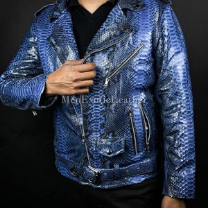 Op de afbeelding: Blau leren jas met een slangenleerpatroon. De jas heeft een reverskraag, meerdere zakken met ritssluiting en een riem in de taille. De tekst "MenExoticLeather" is zichtbaar op de jas.
