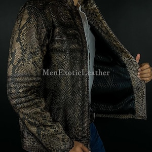 May include: A brown and black snakeskin-effect leather jacket with a zip fastening and a small chest pocket. The jacket is worn over a white shirt and blue jeans. The text "MenExoticLeather" is visible on the jacket.