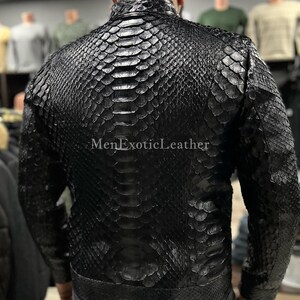 Pode incluir: Casaco de couro preto com padr&atilde;o de pele de cobra. O casaco tem gola alta e fecho de correr. O texto "MenExoticLeather" &eacute; vis&iacute;vel. O casaco parece ser feito de couro de alta qualidade.