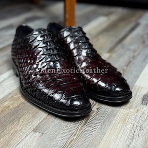 Könnte beinhalten: Ein Paar bordeauxfarbene Lederschuhe mit einem strukturierten, schuppenartigen Muster. Die Schuhe haben schwarze Schnürsenkel und Sohlen. Der Text "MenExoticLeather" ist auf dem Schuh zu sehen.