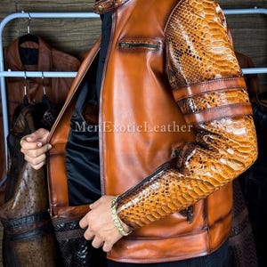 May include: A brown leather jacket with snake skin patterned sleeves and accents. The jacket has a zipper closure and a stand-up collar. The text "MenExoticLeather" is visible on the jacket.