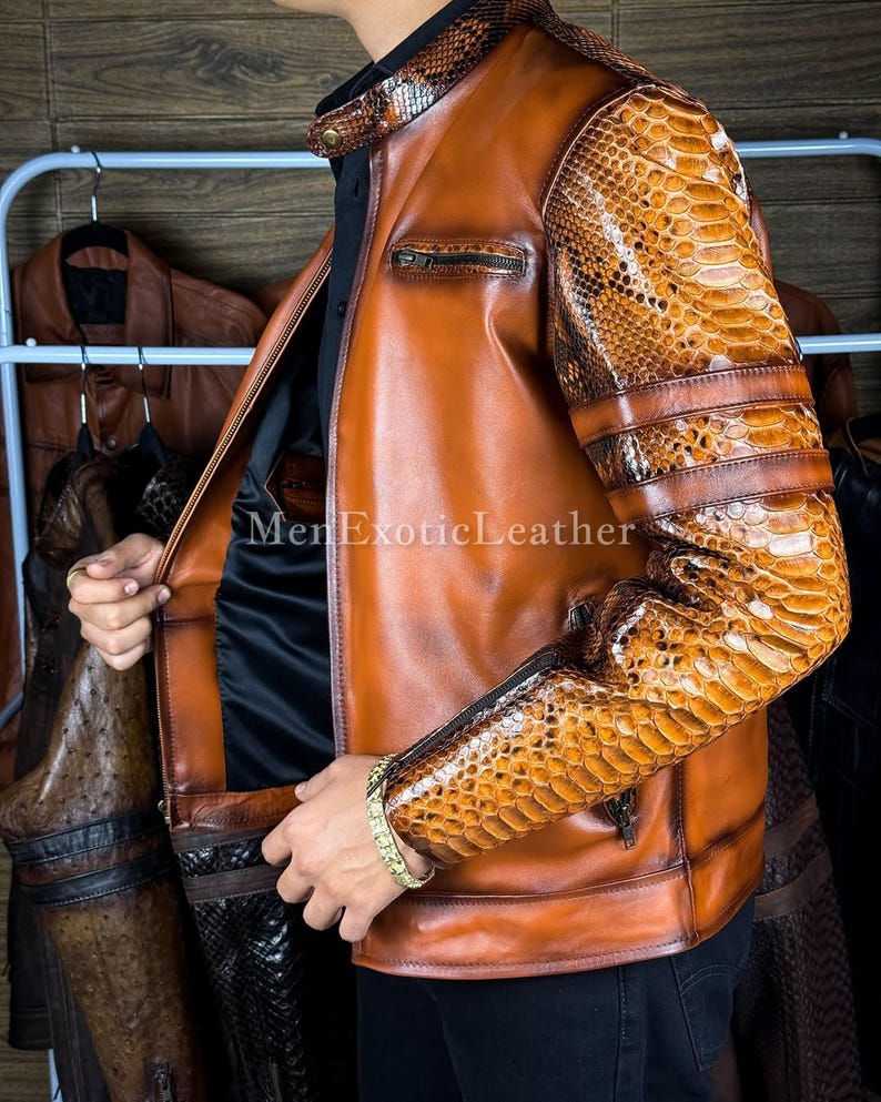 May include: A brown leather jacket with snake skin patterned sleeves and accents. The jacket has a zipper closure and a stand-up collar. The text "MenExoticLeather" is visible on the jacket.