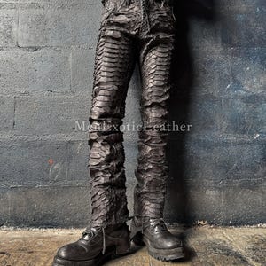 May include: Black, textured leather trousers with a scale-like pattern. The trousers have a fitted design and are paired with black leather boots. The image includes the text "MenExoticLeather".