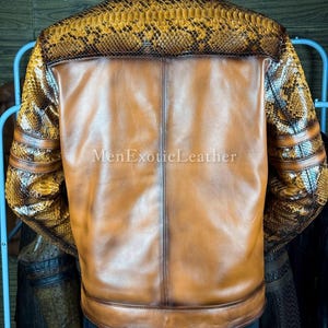 May include: A brown leather jacket with snake skin accents on the shoulders and sleeves. The back of the jacket is a solid brown color. The text "MenExoticLeather" is visible on the lower portion of the jacket.