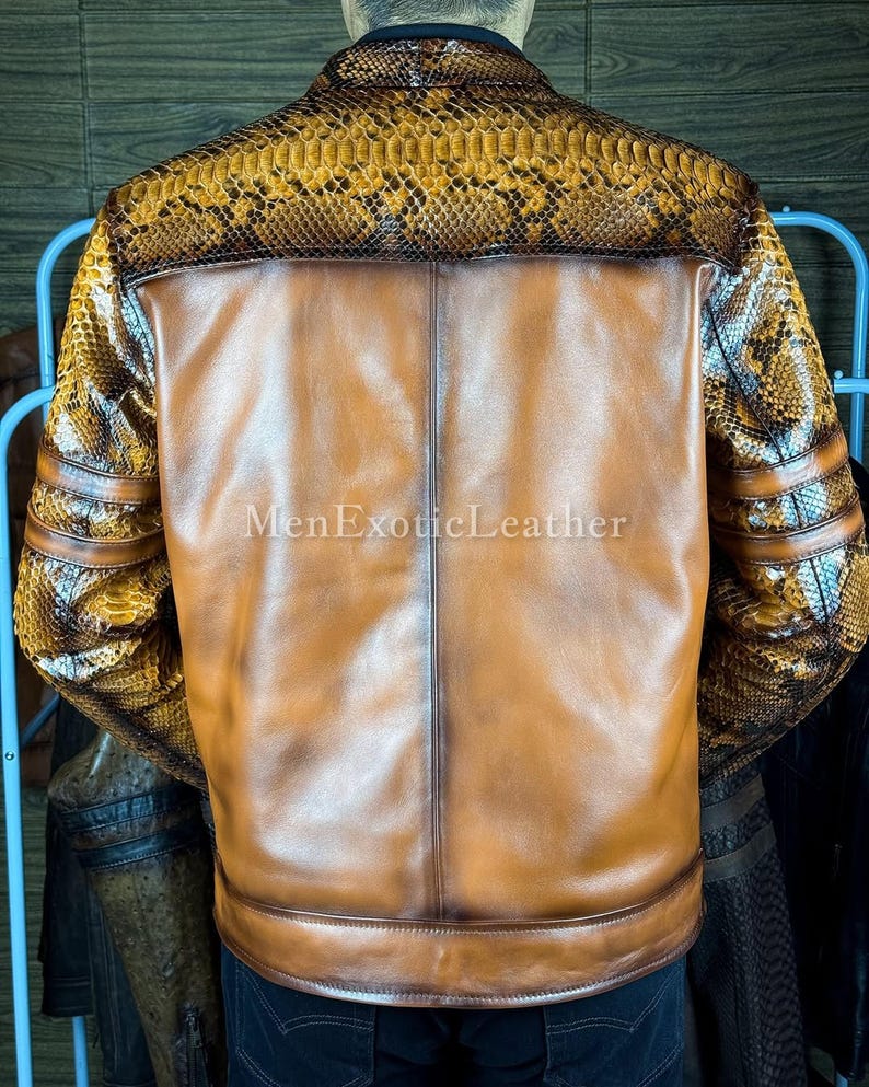 May include: A brown leather jacket with snake skin accents on the shoulders and sleeves. The back of the jacket is a solid brown color. The text "MenExoticLeather" is visible on the lower portion of the jacket.