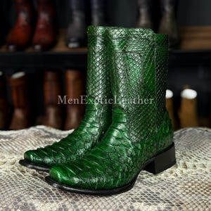 May include: A pair of vibrant green cowboy boots with a textured, reptile-like pattern. The boots have a mid-calf height, a square toe, and a black sole. The boots are displayed on a snakeskin-patterned surface. The text "MenExoticLeather" is visible.
