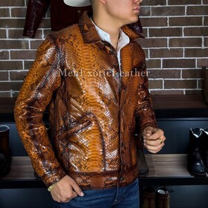 Op de afbeelding: Een bruin en tan slangenleren jasje met een kraag en twee voorzakken. De jas heeft een knoopsluiting en wordt over een wit overhemd gedragen. De tekst "MenExoticLeather" is zichtbaar op de jas.