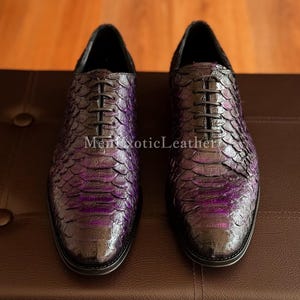 May include: A pair of purple and black leather dress shoes with a snakeskin pattern. The shoes have black laces and a pointed toe. The text "Men Exotic Leather" is visible on the shoe.