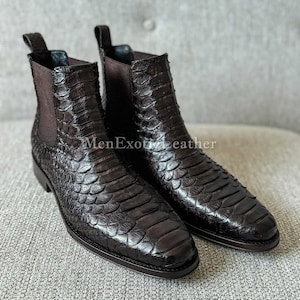 Könnte beinhalten: Ein Paar dunkelbraune Chelsea-Stiefel aus Leder mit einem strukturierten, schuppenartigen Muster. Die Stiefel haben elastische Seiteneinsätze und Zuglaschen. Der Text "MenExoticLeather" ist sichtbar.