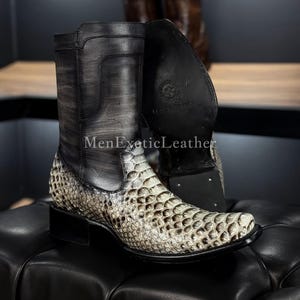 Puede incluir: Botas de vaquero con un patrón de piel de serpiente en la parte inferior y cuero negro en la parte superior. Las botas tienen una punta puntiaguda y un tacón apilado. El texto "MenExoticLeather" es visible en el lateral de la bota.