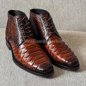 Peut inclure: Une paire de bottines en cuir marron avec un motif texturé et écailleux. Les bottines ont un design à lacets avec des lacets marron et une semelle marron foncé. Le texte "MenExoticLeather" est visible.