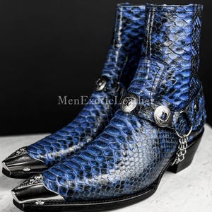 May include: A pair of blue and black snake-skin textured ankle boots with silver metal accents. The boots have pointed toes with silver metal tips, decorative silver buckles, and a small chain detail. The text "MenExoticLeather" is visible.