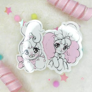 May include: Two white cartoon stickers of dogs with pink accents. One dog is wearing a bow and the other is wearing a bow and a scarf. The stickers are on a white fuzzy background with pink and iridescent confetti.