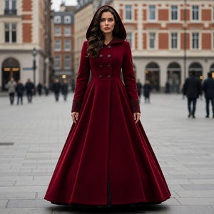 May include: A floor-length, deep burgundy coat featuring a structured hood, long sleeves with cuffs, and a double-breasted front closure with dark buttons. The garment has a fitted bodice that transitions into a full, flared skirt silhouette.