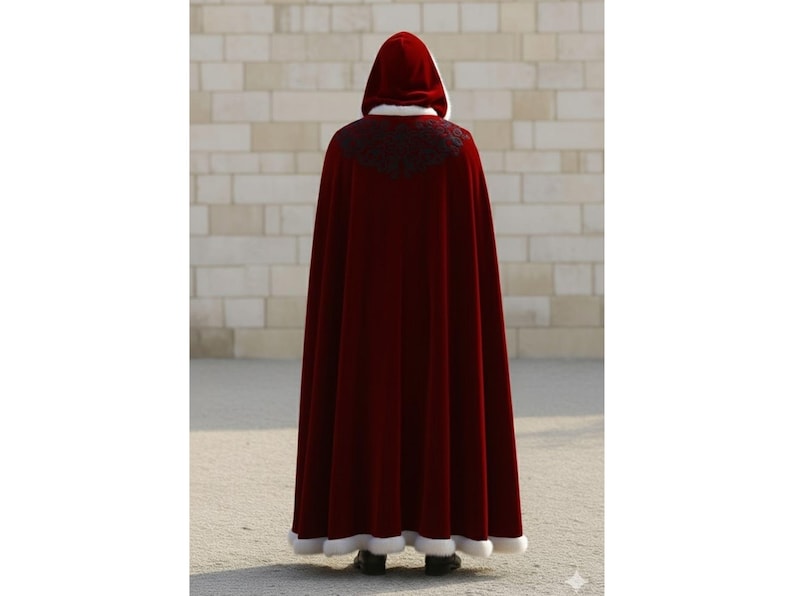 May include: A long, burgundy velvet cloak with a hood, white trim, and black embroidered detailing at the shoulders. The cloak is floor-length and worn by a person facing away from the camera.