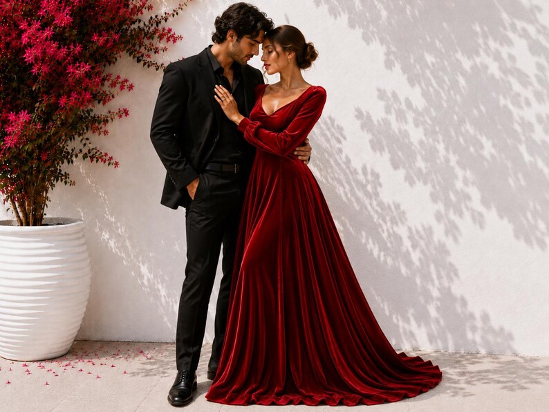 May include: A long-sleeved, floor-length velvet gown in a deep red hue featuring a V-neckline and a full, flowing skirt, paired with a black suit consisting of a tailored blazer, matching trousers, and a dark button-down shirt.