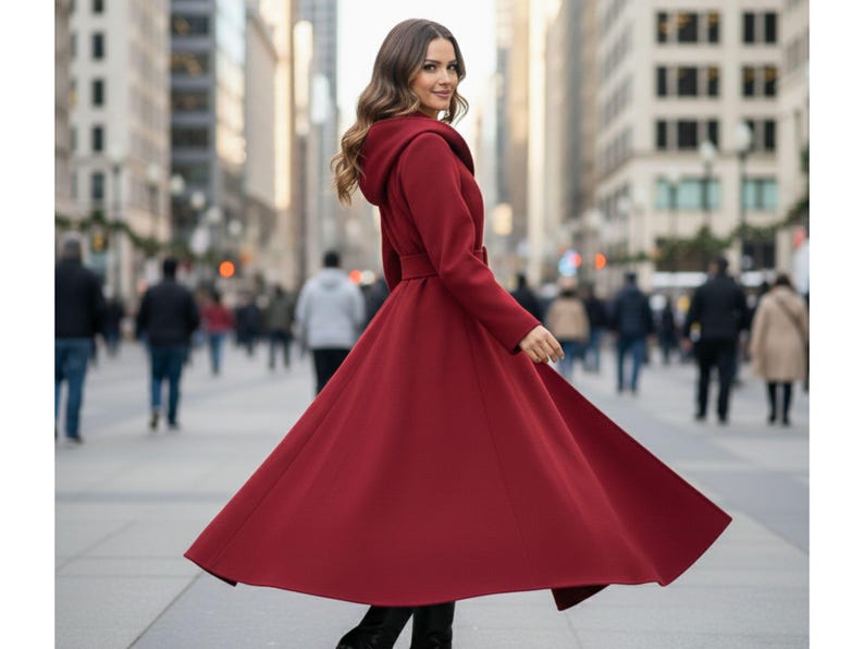 May include: A long, flowing red coat with a hood and belt, worn outdoors. The coat is a deep shade of red and has a flared skirt. The person is walking on a city street.