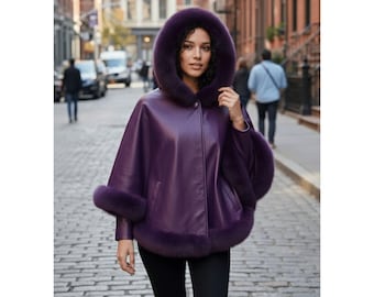 May include: A purple leather cape with a fur-lined hood and cuffs. The hooded cape has a button closure and is worn over black pants. The image is taken on a cobblestone street with people and cars in the background.
