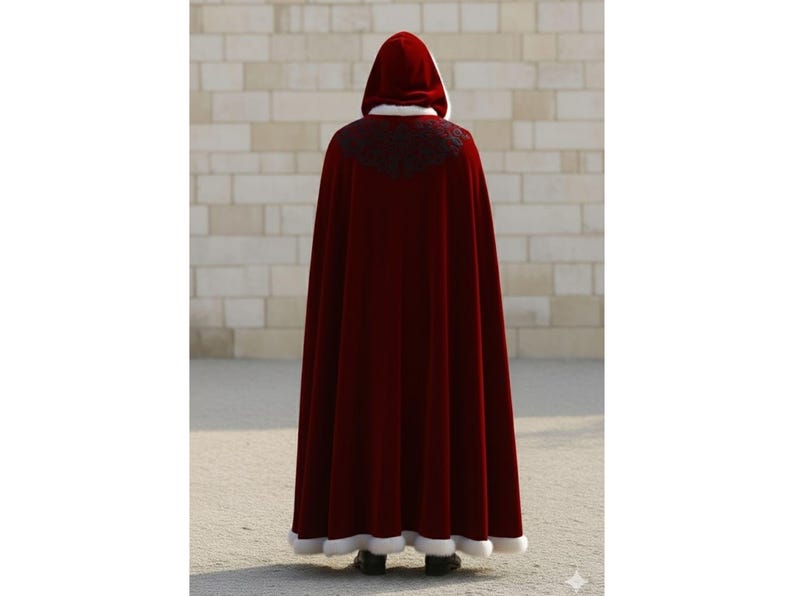 May include: A long, burgundy velvet cloak with a hood, white trim, and black embroidered detailing at the shoulders. The cloak is floor-length and worn by a person facing away from the camera.