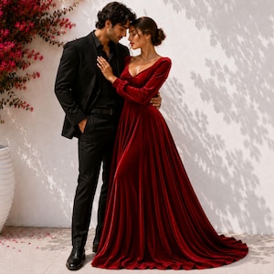 May include: A floor-length, long-sleeved velvet dress in a deep red hue featuring a V-neckline and a full, flowing skirt, paired with a black suit consisting of a tailored blazer, matching trousers, and a dark shirt worn underneath.