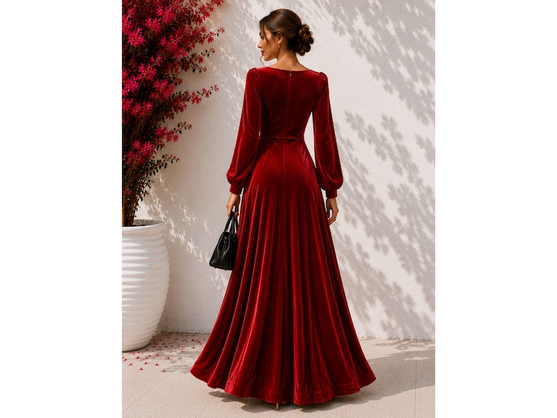 May include: A floor-length, deep red velvet dress featuring long, full sleeves with fitted cuffs, a defined waistline, and a flowing, pleated skirt. The garment has a simple, solid-colored design with a smooth texture and a back zipper closure.