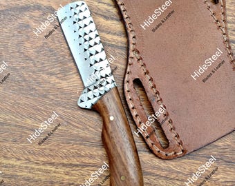 Puede incluir: Un cuchillo artesanal con mango de madera y hoja de acero estampada. El cuchillo va acompañado de una funda de cuero marrón. La hoja presenta una serie de recortes triangulares. El mango es de color marrón oscuro.