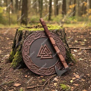Könnte beinhalten: Ein Wikinger-Schild- und Axt-Set. Der Schild ist braun mit einem kreisförmigen Design und einem zentralen Symbol. Die Axt hat einen Holzgriff und eine dunkle Metallklinge. Das Set wird auf einem Baumstumpf in einem Wald dargestellt.