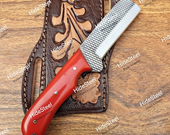 Könnte beinhalten: Ein Messer mit rotem Griff und strukturierter Klinge liegt auf einer braunen Lederscheide mit floralen Verzierungen. Das Messer hat eine silberne Klinge und ist mit "HideSteel Blades & Leather" beschriftet. Die Scheide ist ebenfalls braun.