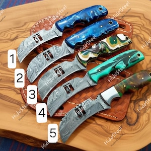 May include: Five Damascus steel knives with curved blades and colourful handles. The handles are blue, green, and brown, with a marbled effect. The blades have a unique pattern. The knives are displayed on a wooden surface.