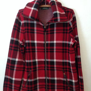 May include: Red, black and white plaid zip-up jacket with a high collar. The jacket has two pockets on the front and the brand name "LAUREN" is visible on the left side of the zipper.