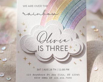 May include: A light-colored invitation card with a rainbow and cloud design. The text reads "WE ARE OVER THE rainbow" and "Olivia IS THREE". Additional text includes the date, time, address, and RSVP information. Gold star accents are scattered around the design.