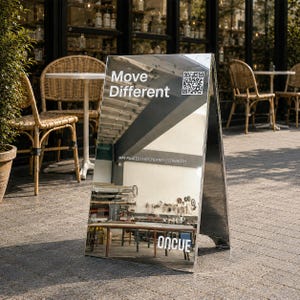 Op de afbeelding: Een zilverkleurig A-bord met een reflecterend oppervlak. Het bord bevat de witte tekst Move Different, een QR-code, de tekst Mat Pilates | Hot Pilates | Strength en de witte logotekst ONCUE gedrukt op het gespiegelde oppervlak.