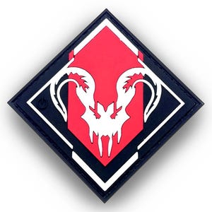 May include: A black, square patch featuring a red diamond with a white stylized skull design. The patch has a black border with a white and black inner border. The design is a gaming emblem.