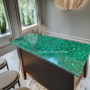 May include: A rectangular, dark brown wooden table with a vibrant green malachite top. The table is in a well-lit room with a marble floor and a large window. The text "FinestFurnitureStore" is visible on the table.
