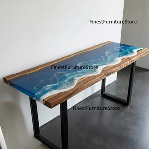 May include: A wooden desk with a blue and white resin design resembling ocean waves. The desk has a dark wood frame and black metal legs. The text "FinestFurnitureStore" is visible on the desk.