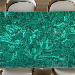 May include: Rectangular malachite table with a vibrant green and dark green pattern. The table is surrounded by four white chairs with wooden frames. The table's surface has a polished, natural stone appearance, showcasing unique veining.