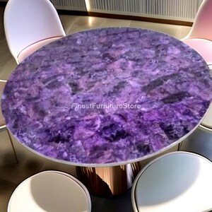 Könnte beinhalten: Ovaler Esstisch mit einer Tischplatte aus violettem Amethyststein. Der Tisch hat ein kupferfarbenes Gestell und ist von weißen und rosa Stühlen umgeben. Der Text "FinestFurnitureStore" ist sichtbar.