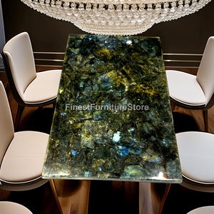 May include: A rectangular dining table with a polished, multi-coloured stone top, featuring shades of green, gold, and blue. The table is surrounded by white chairs and is beneath a crystal chandelier. The text "FinestFurnitureStore" is visible.
