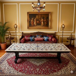 May include: A rectangular marble-topped coffee table with a black base, featuring intricate floral patterns in blue, red, and white. The table sits on a large red and cream patterned rug, with a dark wooden sofa and a painting in the background.