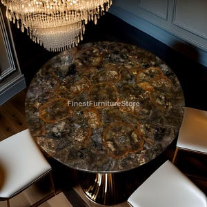 Puede incluir: Una mesa de comedor redonda con una encimera de piedra única con patrones marrones y dorados. La mesa tiene una base de pedestal dorada y está rodeada de sillas blancas. El texto "FinestFurnitureStore" es visible en la superficie.