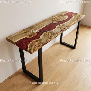May include: A rectangular wooden console table with a live edge design. The tabletop features a river of deep red epoxy resin flowing through the natural wood grain. The table is supported by black metal legs.