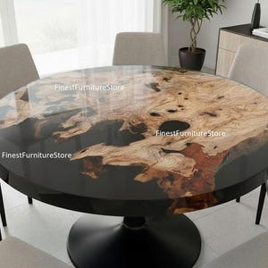 Op de afbeelding: Een ronde eettafel met een zwarte voet en een uniek tafelblad met houtnerf. Het tafelblad heeft een glanzende afwerking met natuurlijke houtpatronen in bruin- en beigetinten. De tafel is omringd door stoelen in neutrale kleuren.