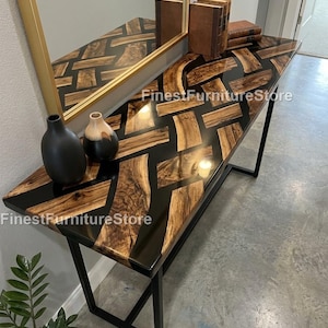 May include: A modern console table with a black epoxy resin and wood inlay top. The table has a black metal frame and is decorated with vases, books, and a mirror. The table's dimensions are not visible in the image.
